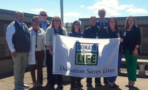 Sen. Hutchinson standing with a group of individuals holding a Donate Life - Donation Saves Lives flag.