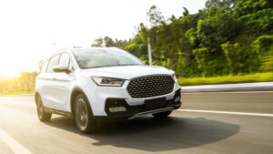 Late model white SUV in motion on asphalt highway with green trees and vegetation in background.