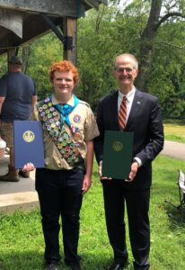 Senator Hutchinson Alt Text Eagle Scout smiling at camera and holding House and Senate citations.