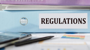 Blue binder labeled “Regulations” sitting on desk with pen, calculator and paperwork.